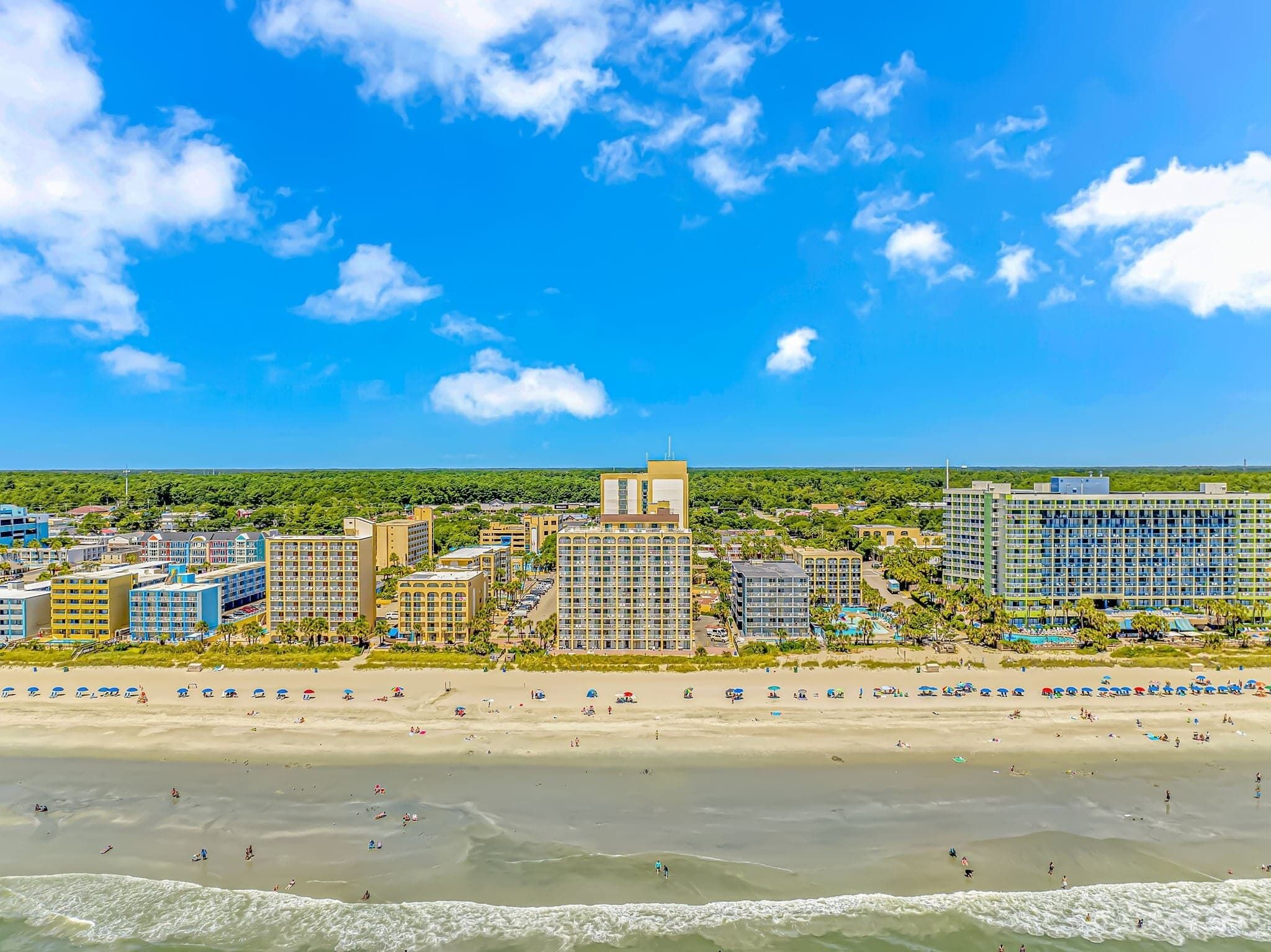A coastal resort with multiple high-rise buildings, a sandy beach, and a clear blue sky.