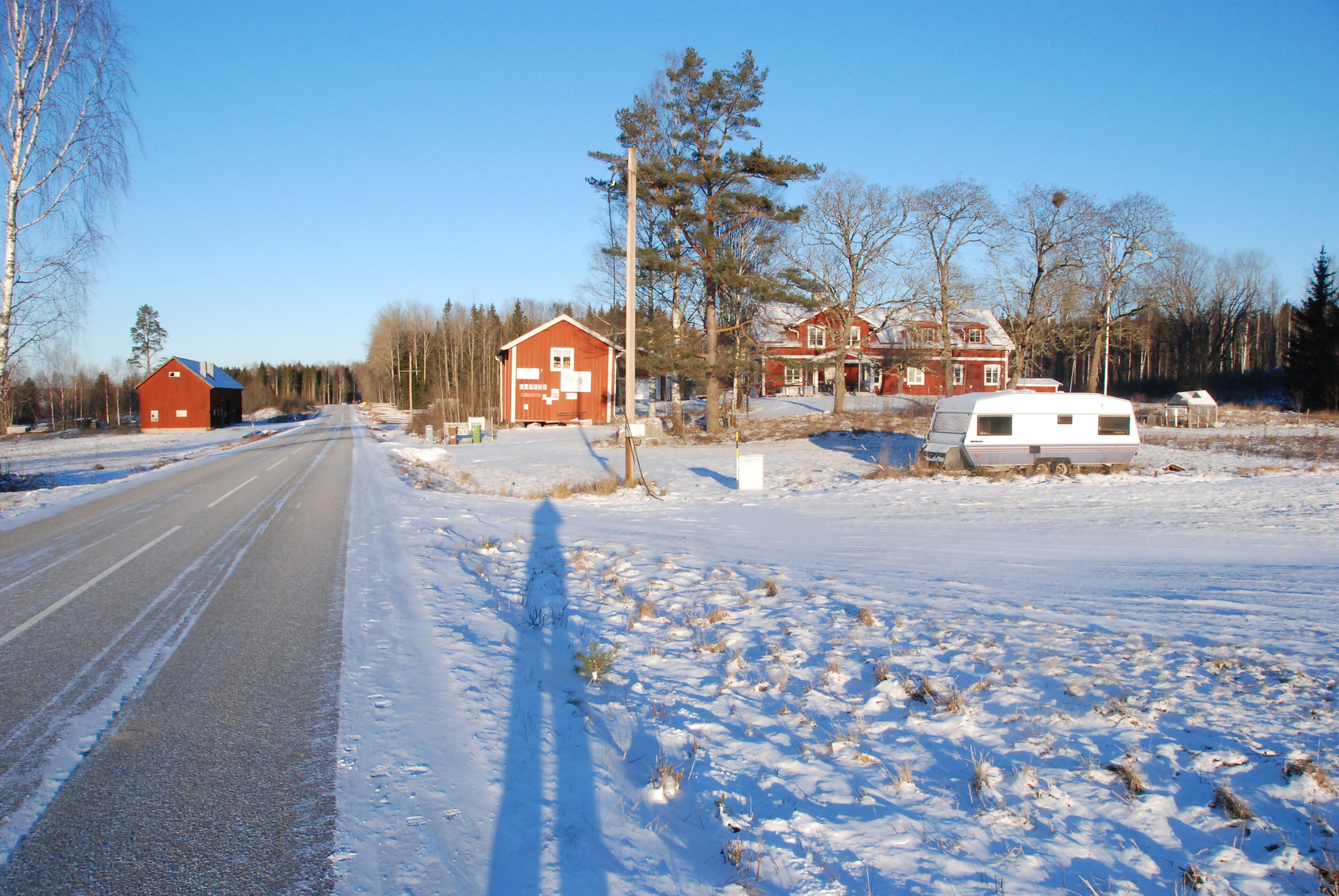 En landsväg med ett snötäckt landskap, en röd lada och en vit husvagn.