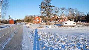 En landsväg med ett snötäckt landskap, en röd lada och en vit husvagn.