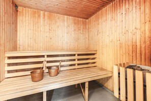 A wooden sauna with a bench, two metal buckets, and a wood-burning stove. - Solmyra 56 Gästhem (Kolsva)