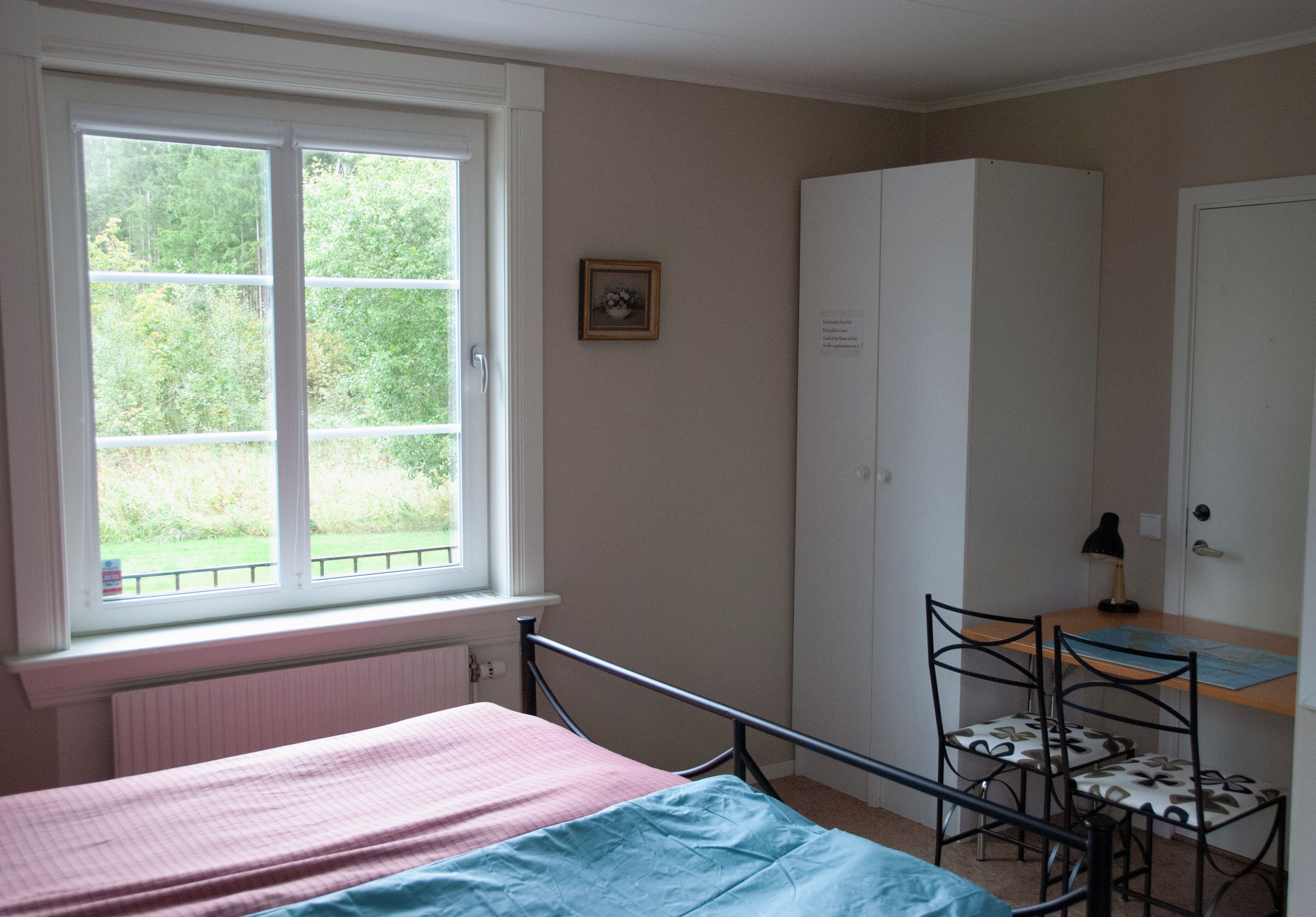 Un dormitorio con cama, ventana, armario, escritorio con silla y una mesita.