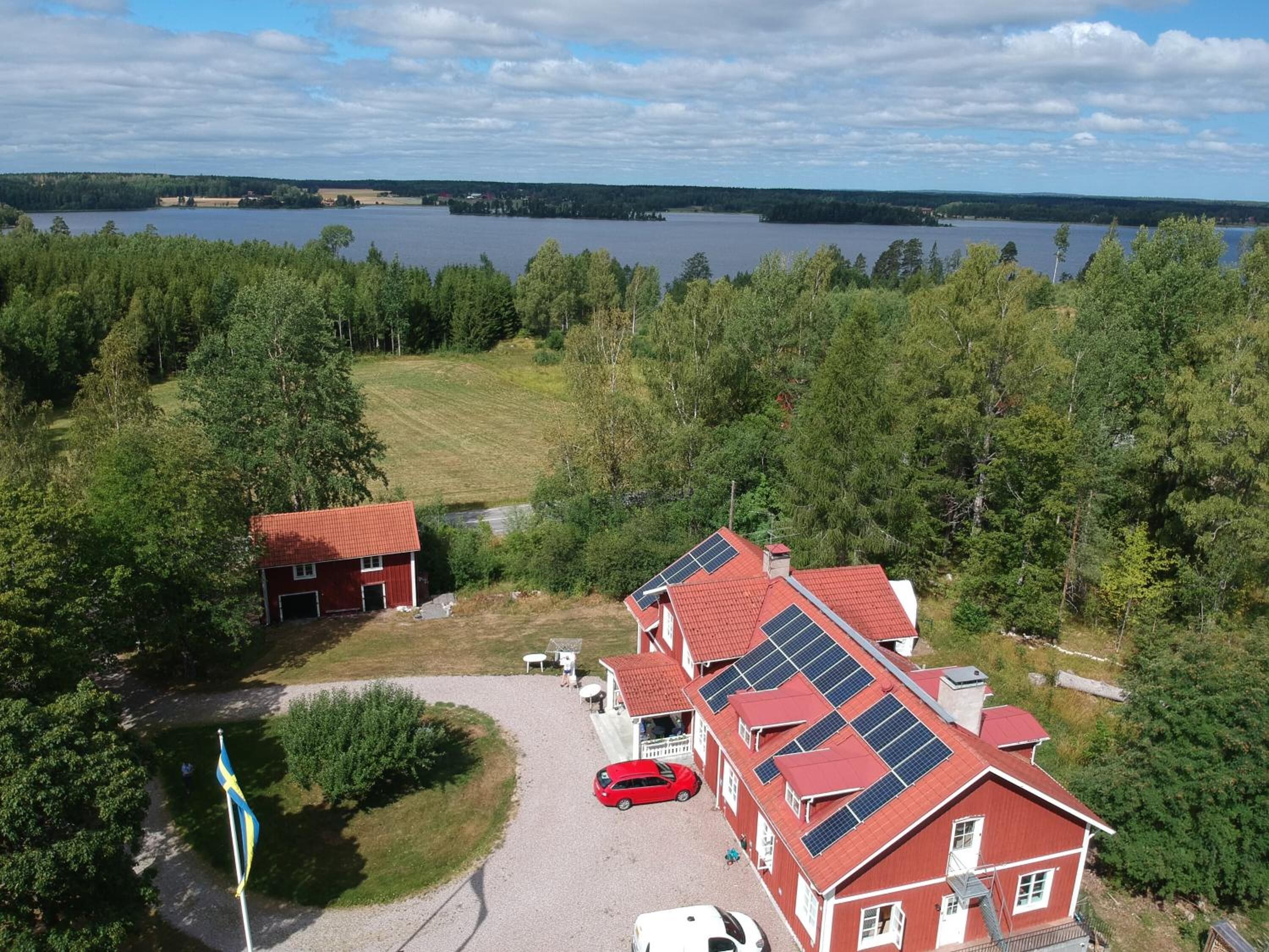 Edificio de techo rojo con paneles solares, rodeado de árboles y un lago.