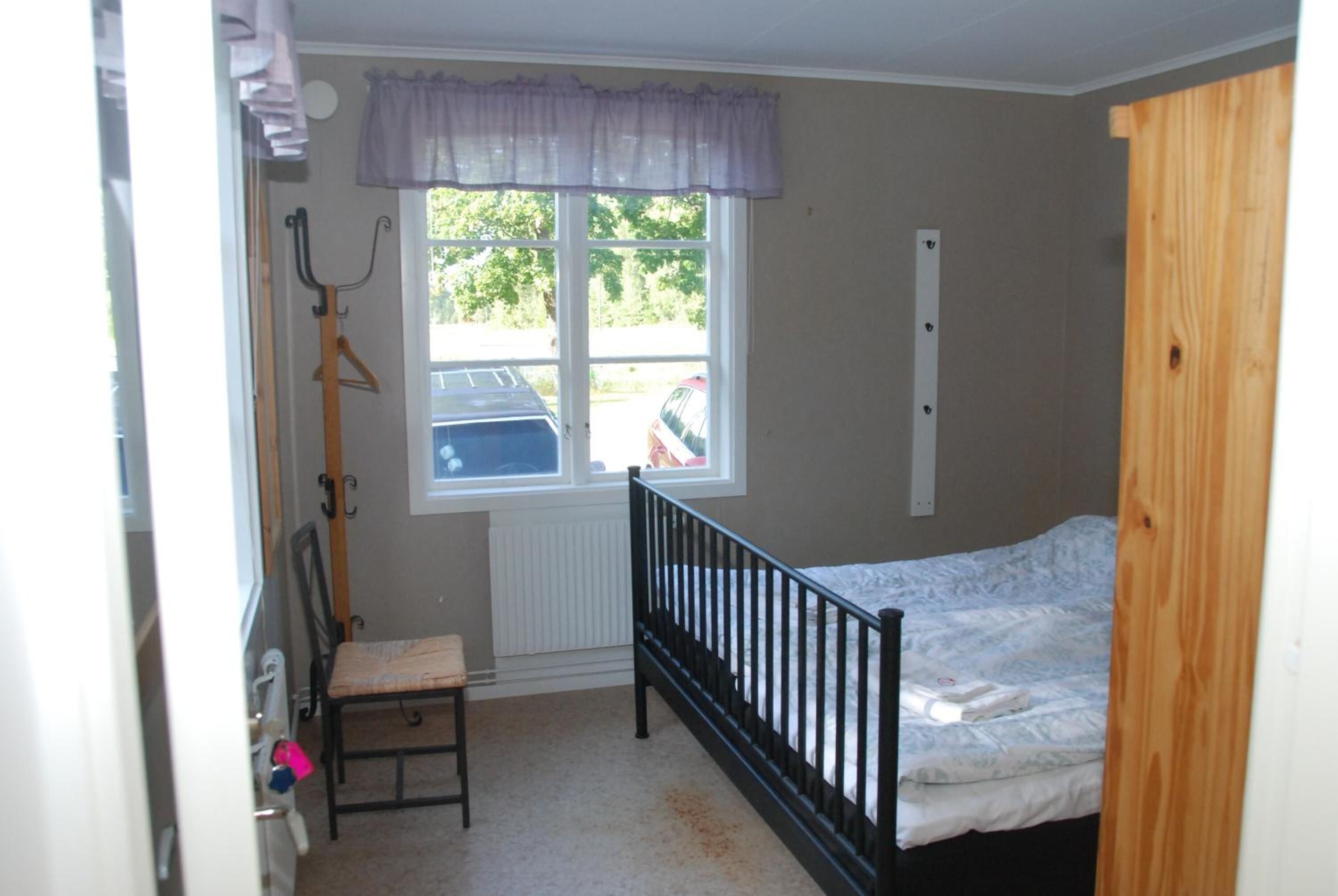 Un dormitorio con una cama individual, una ventana, un radiador, una silla y un perchero.