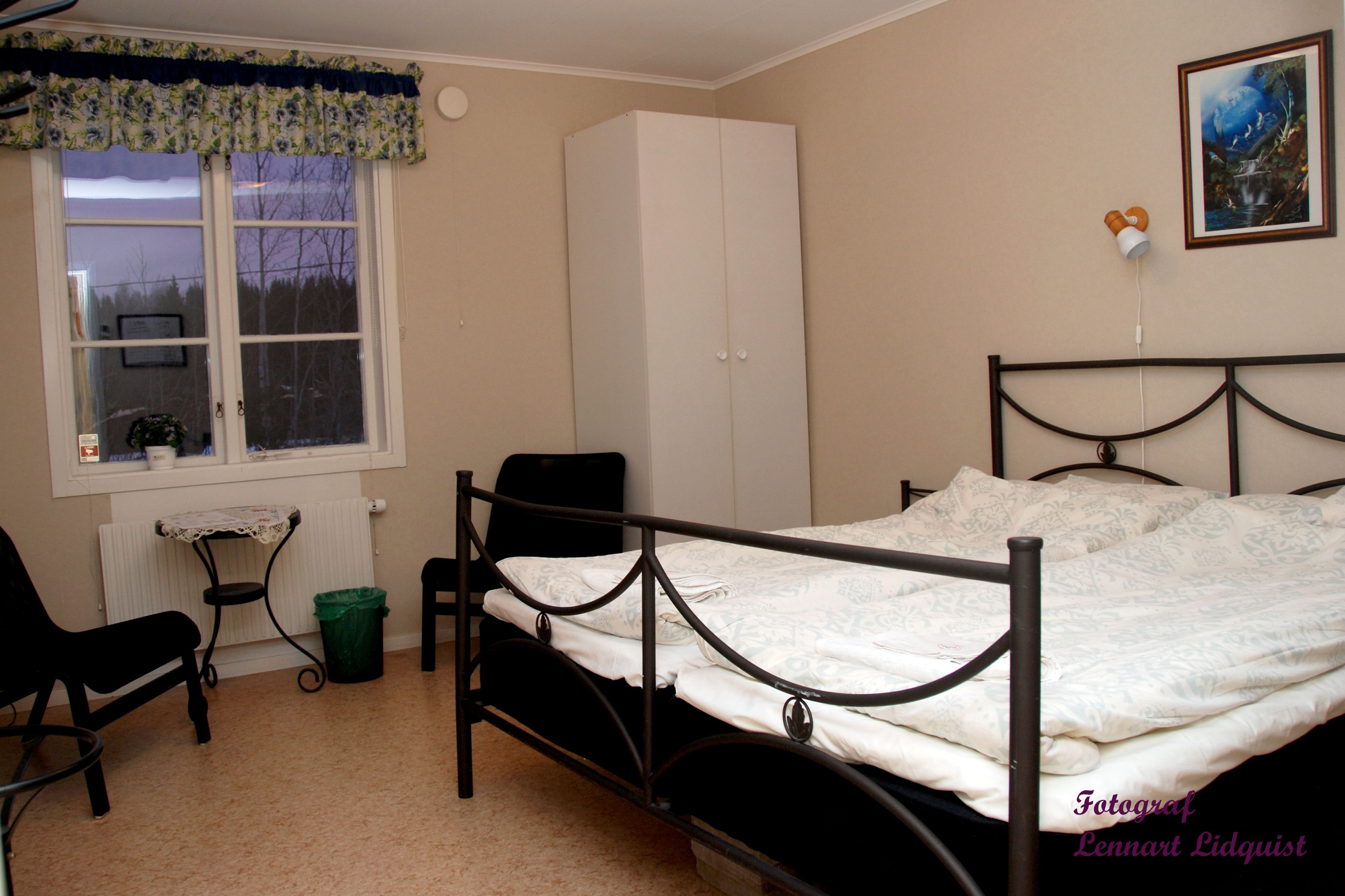 A bedroom with a bed, a chair, a radiator, a window with a curtain, a wardrobe, and a picture on the wall.