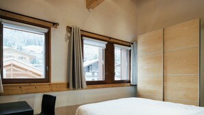Un dormitorio con cama, escritorio y dos ventanas.