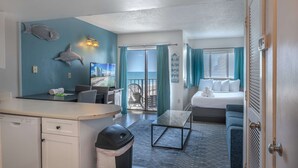 Une chambre comprenant un lit, un bureau, une chaise, une poubelle et une vue sur l’océan, accessible par une porte coulissante.