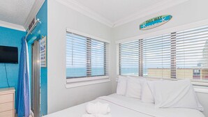 Une chambre d’hôtel avec un lit, une fenêtre avec des stores, une serviette sur le lit et un panneau au-dessus de la fenêtre.