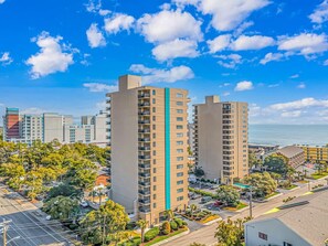 A high-rise building with multiple floors, surrounded by greenery and a clear blue sky.