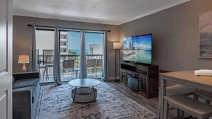 A hotel room with a balcony, a television, a sofa, a dining table, and a fireplace. - Ocean Dunes Tower II - Unit 6044 (Myrtle Beach)