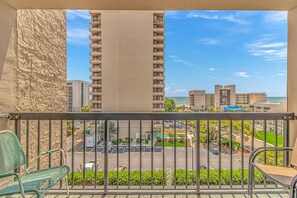 A balcony with a view of a parking area, a pool, and high-rise buildings.