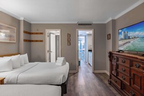Ein Hotelzimmer mit einem großen Bett, einem Schminktisch, einem Fernseher und Blick auf den Strand.