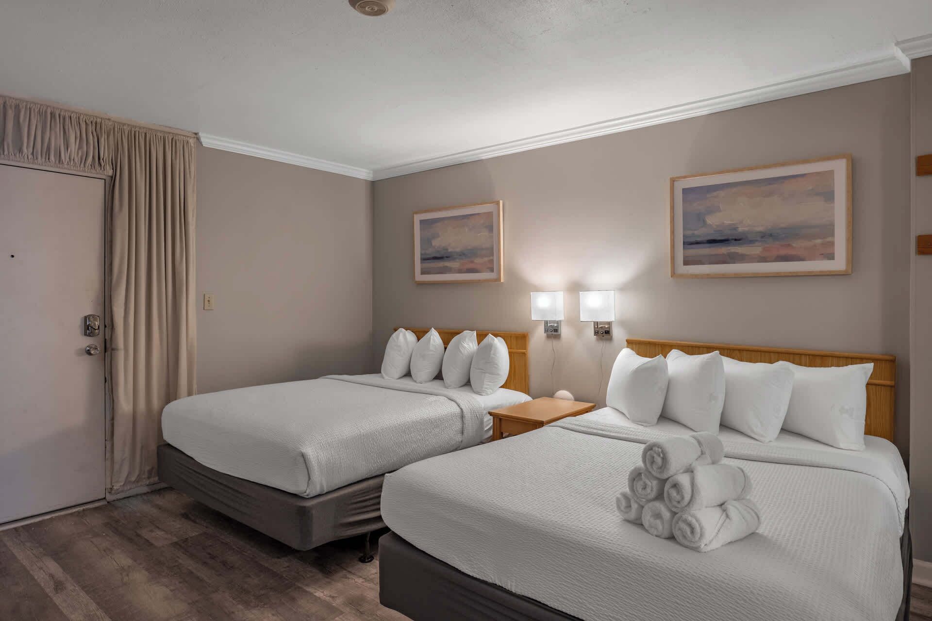 A hotel room with two beds, a wooden headboard, a nightstand, and two wall-mounted lamps.