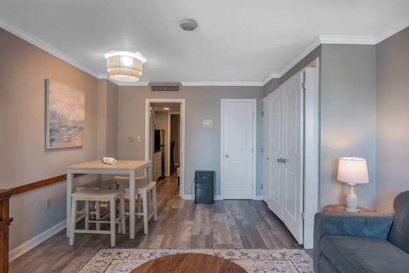 A hallway with a dining table, chairs, a lamp, and a couch.
