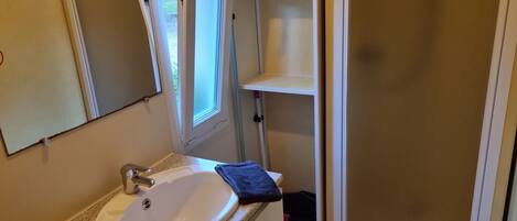 A bathroom with a white sink, a mirror, a window, and a shower area.