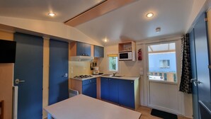 Une cuisine compacte avec des meubles bleus, un plan de travail blanc, une cuisinière, un four à micro-ondes et une fenêtre donnant sur un bâtiment à l’extérieur.