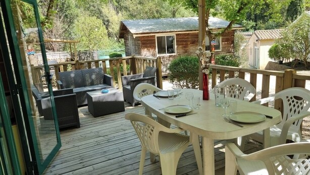 Une terrasse en bois avec une table dressée pour le repas, des meubles en osier et une vue sur un chalet.