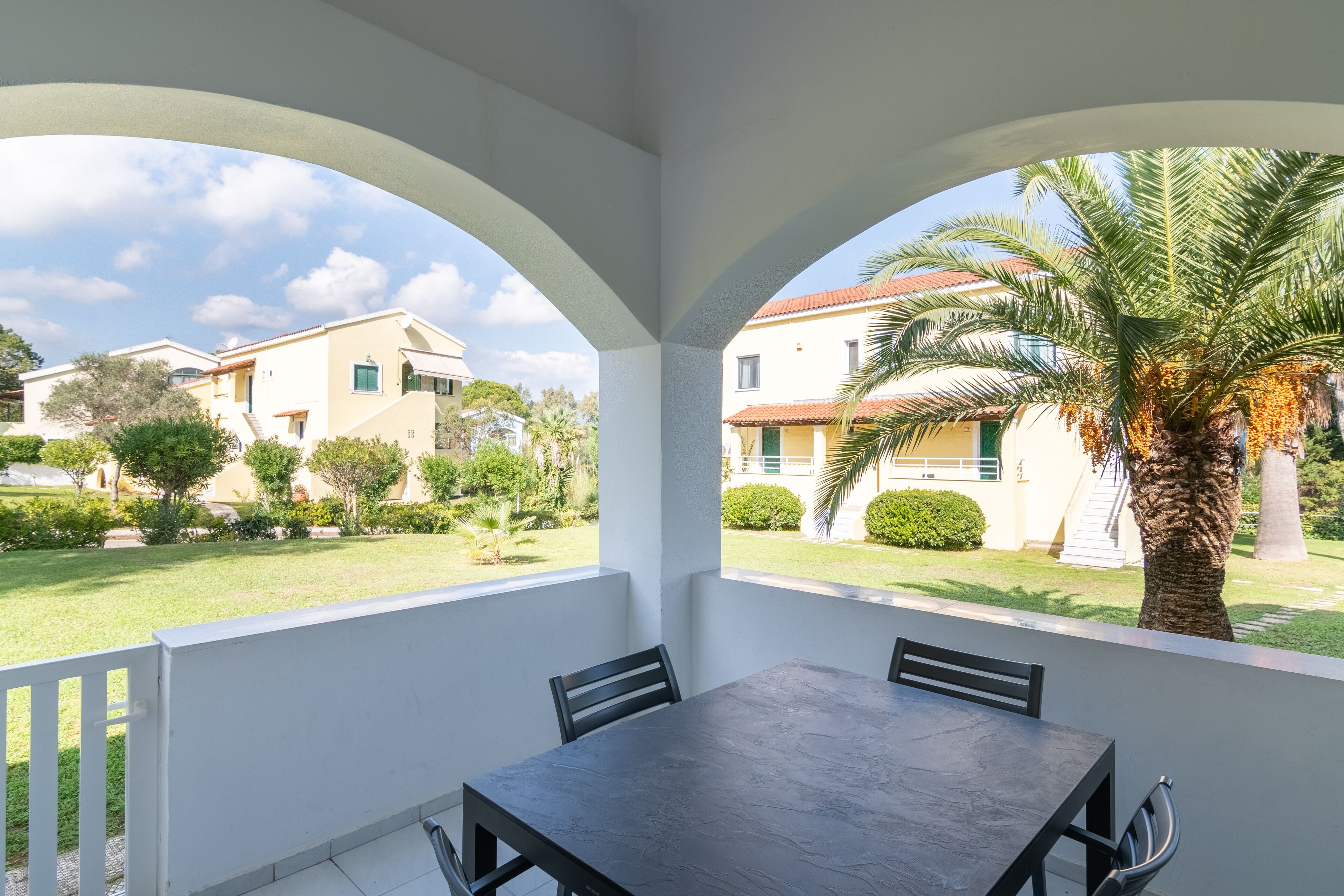 A balcony with a table and chairs, overlooking a residential area with houses and a palm tree.