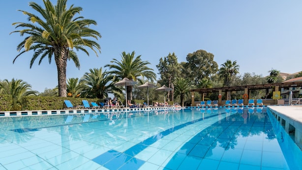 A swimming pool with blue tiles, surrounded by palm trees and lounge chairs. - Helion Resort (Corfu)