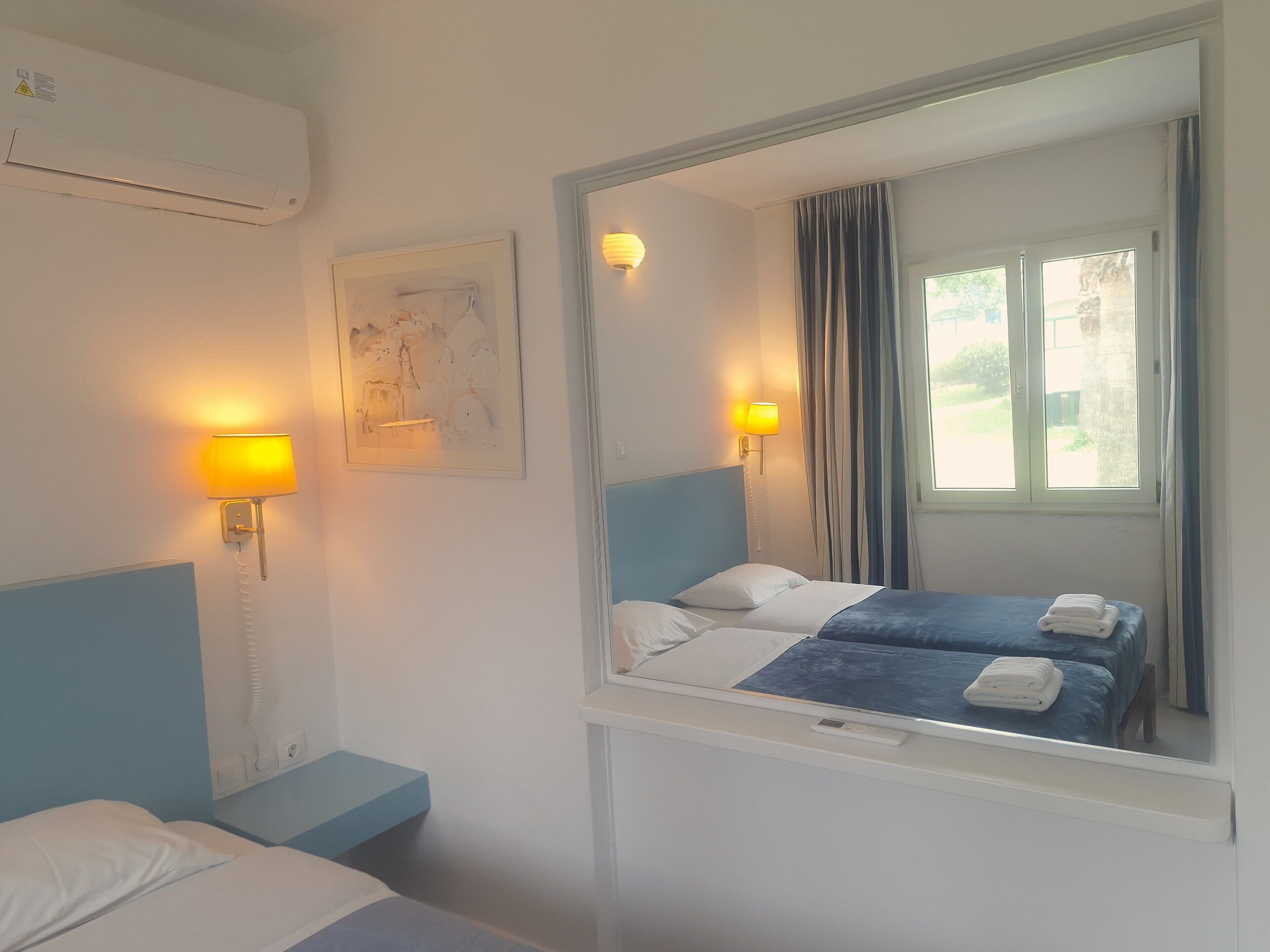 A hotel room with a bed, bedside lamps, a mirror, and a window with curtains.