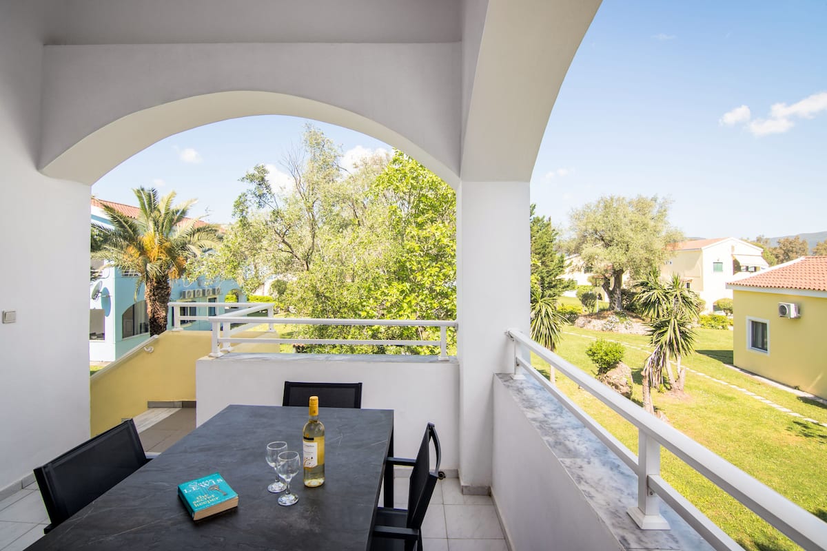 Ein Balkon mit Tisch, Stühlen, einem Buch und einer Weinflasche.