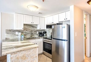 A modern kitchen with white cabinets, a marble countertop, a stainless steel refrigerator, and a built-in oven.