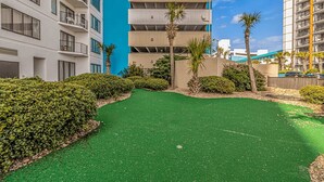 A courtyard with artificial green turf, palm trees, and a building with balconies. - Palace 2206 (Myrtle Beach)