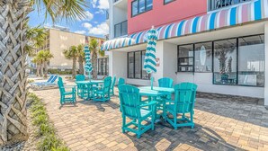 A hotel patio with outdoor seating, palm trees, and a striped awning. - Palace 2206 (Myrtle Beach)