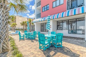 Une terrasse d’hôtel avec des places assises en plein air, des palmiers et un auvent à rayures.