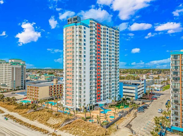 A high-rise hotel with multiple floors, a swimming pool, and a parking area.