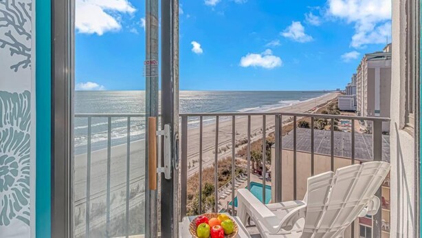 Balcón con vista a la playa y al océano, una silla y un frutero.