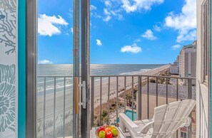 A balcony with a view of the beach and ocean, a chair, and a fruit bowl. - Palace 705 (Myrtle Beach)