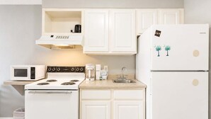 A compact kitchen with white cabinetry, a microwave, a stove, a coffee maker, and a refrigerator. - Sea Mist 50809 (Myrtle Beach)