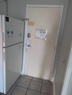 Una puerta con un cartel que indica un plan de evacuación, un refrigerador decorado con palmeras y un piso de baldosas.