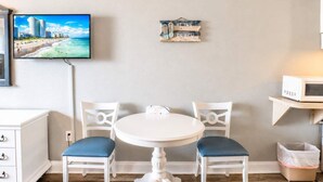 A room with a white table and chairs, a television mounted on the wall, and a beach-themed sign. - Sea Mist 50809 (Myrtle Beach)