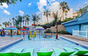A water park with multiple water features, including slides and water jets, surrounded by palm trees and a pool area with lounge chairs. - Coral Beach 816 LOP (Myrtle Beach)