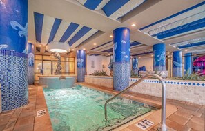 An indoor pool with blue-tiled walls and columns, a hot tub, and a clear water feature. - Coral Beach 816 LOP (Myrtle Beach)
