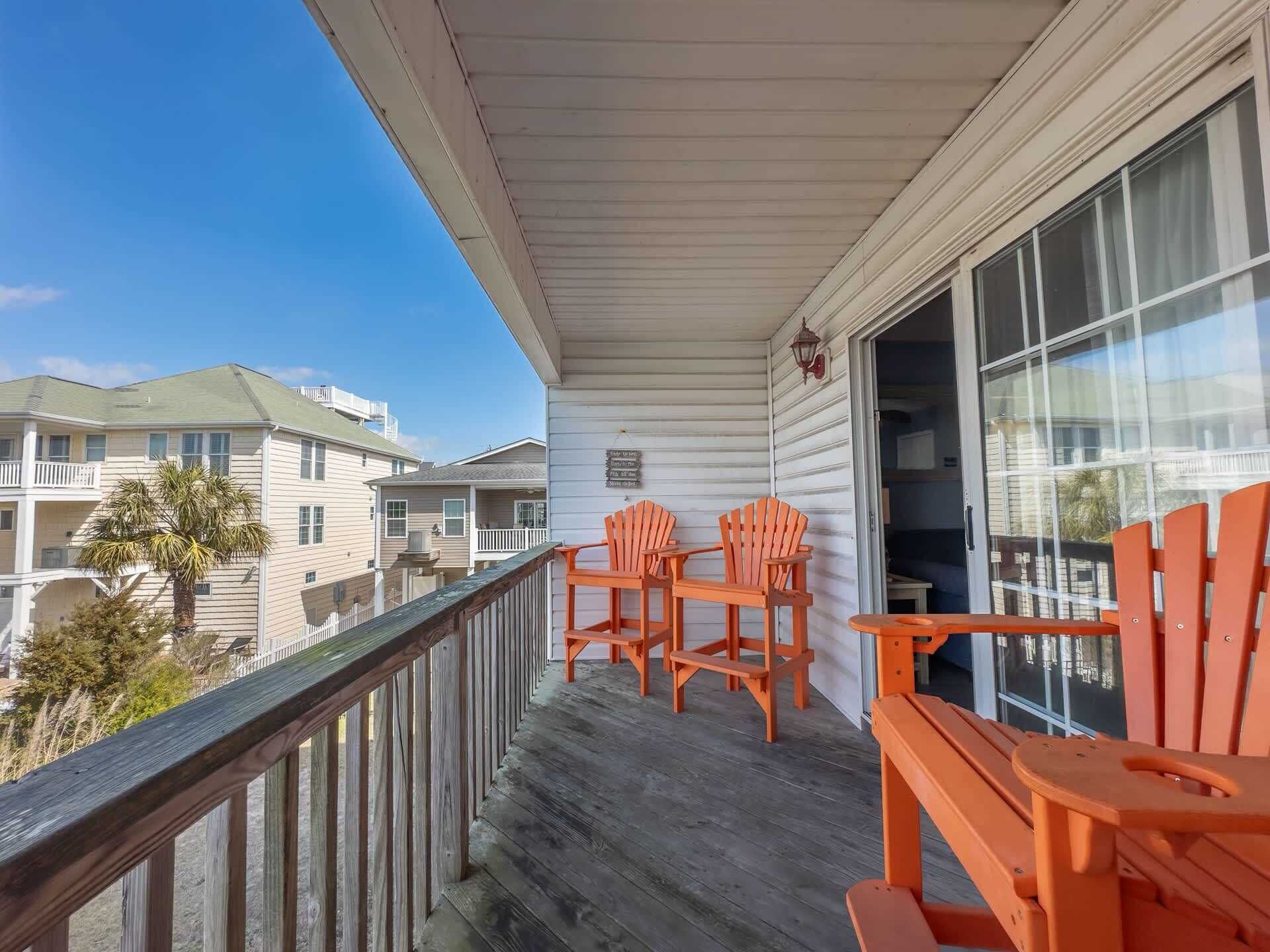A balcony with wooden railings, two orange Adirondack chairs, and a view of neighboring buildings.