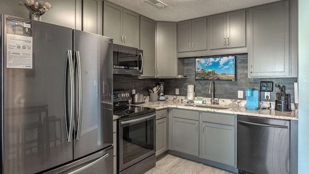 A modern kitchen with stainless steel appliances, grey cabinets, a built-in oven, and a coffee maker. - Sea Pond Villa Unit 3 (North Myrtle Beach)
