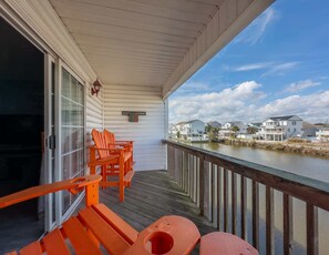 A covered deck with wooden chairs and benches, a view of houses across a body of water, and a clear sky. - Sea Pond Villa Unit 3 (North Myrtle Beach)