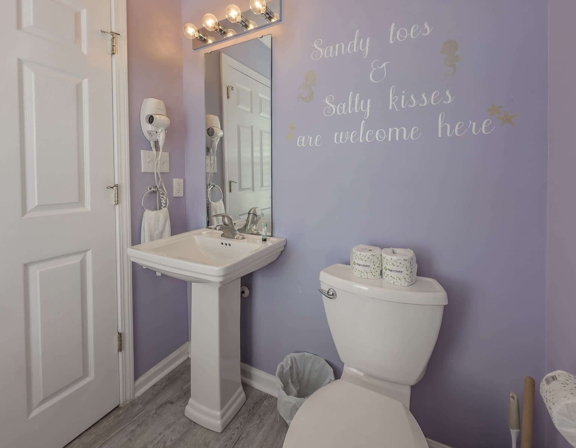 Un baño con un lavamanos pedestal, un inodoro y una pared con un mensaje de bienvenida.
