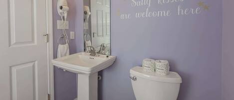 Un baño con un lavamanos pedestal, un inodoro y una pared con un mensaje de bienvenida.