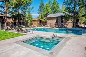 A swimming pool with lounge chairs and a hot tub, surrounded by trees and buildings.