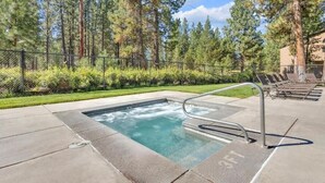 Un jacuzzi con una escalera metálica, rodeado por un suelo de hormigón y una valla de malla.