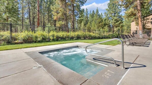 A hot tub with a metal ladder, surrounded by a fence and trees.