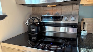 Una cocina de acero inoxidable con horno empotrado y estufa, una tetera y un electrodoméstico KitchenAid en la encimera.