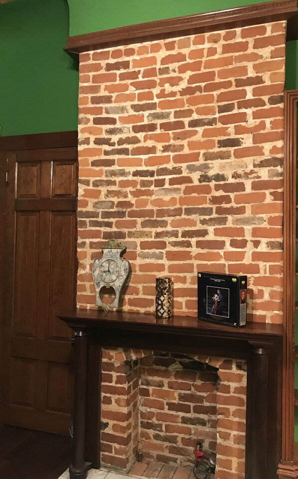 Une cheminée en briques surmontée d’une étagère où sont exposés une horloge, un vase décoratif et un tableau encadré.