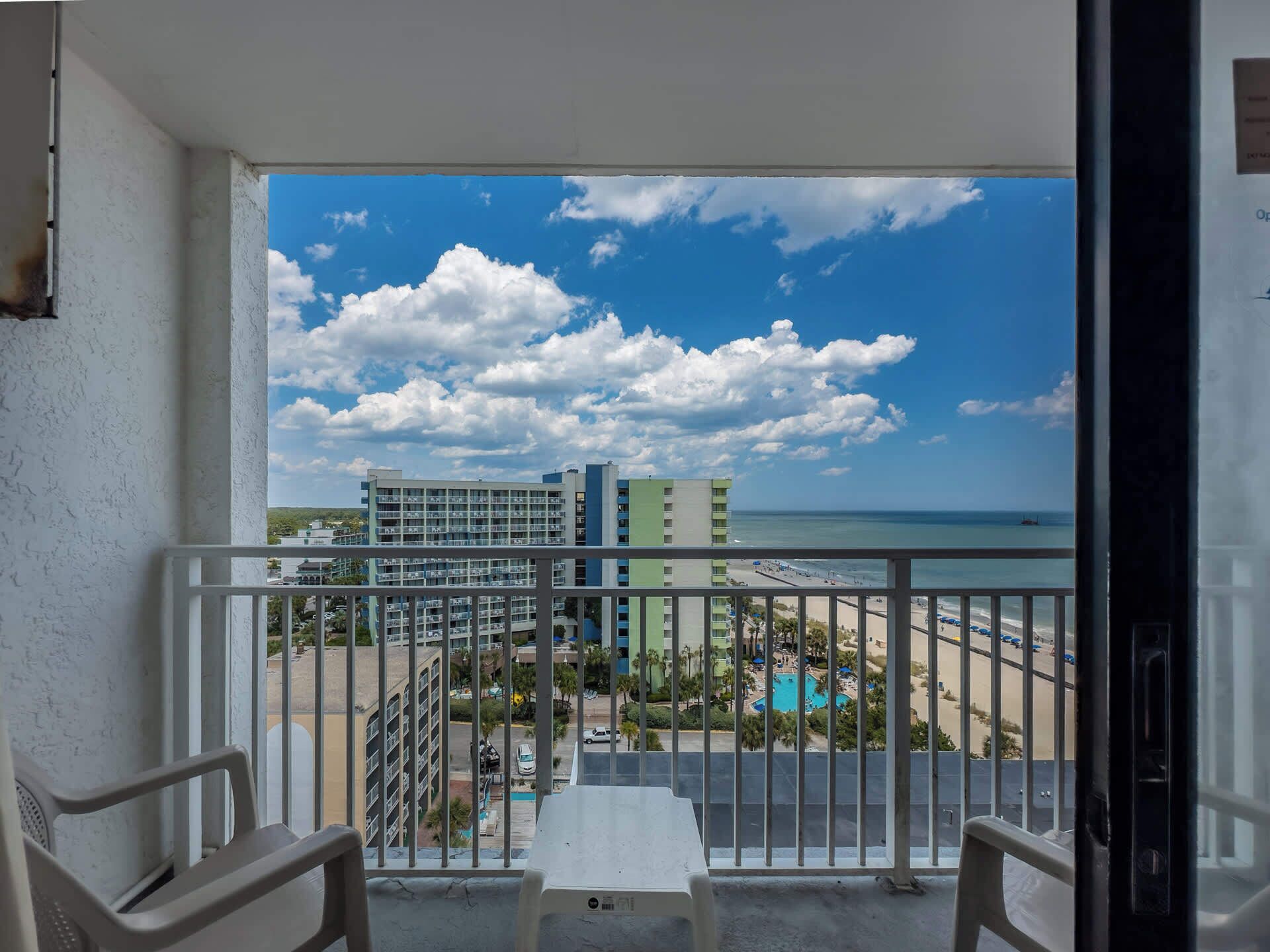 A balcony with a view of a beach, a pool, and a hotel building.