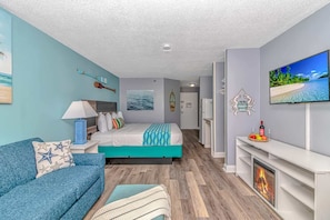 Una habitación de hotel moderna con cama, sofá, televisor, chimenea y vista al mar.