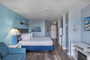 A hotel room with a bed, a desk, a chair, a lamp, and a painting of a beach scene.