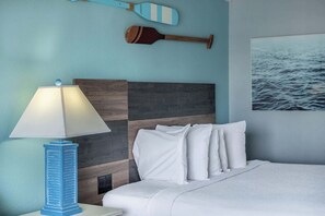 A bedroom with a bed, a nightstand, a lamp, a wall-mounted paddle, and a framed picture of water.